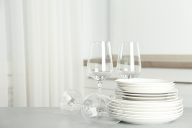 Photo of Stack of clean plates and glasses on grey table in kitchen. Space for text