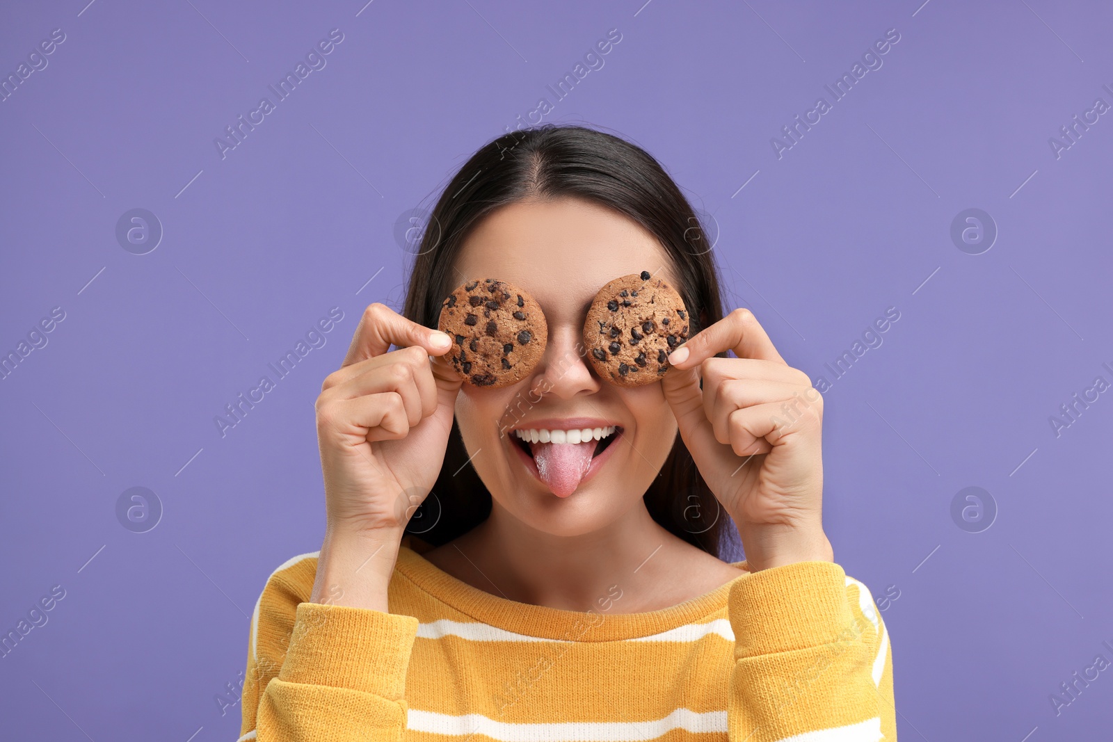 Photo of Young woman with chocolate chip cookies on purple background