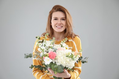 Beautiful woman with bouquet of flowers on grey background