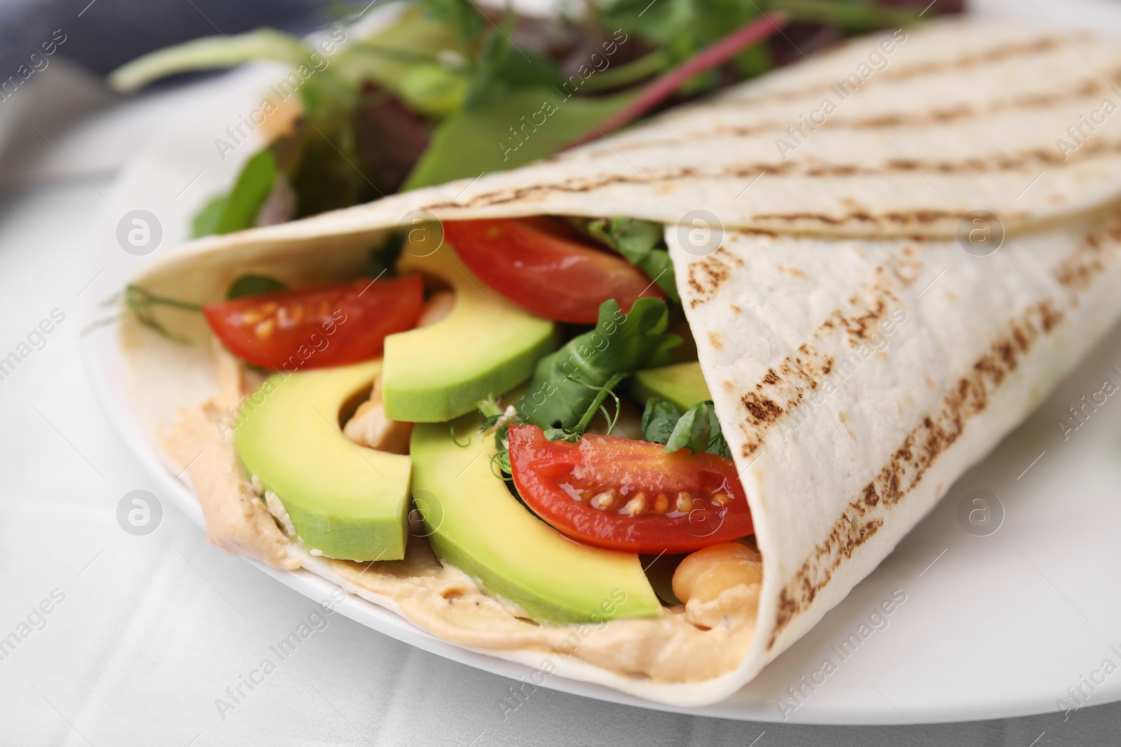 Photo of Plate with hummus wrap and vegetables on white table, closeup