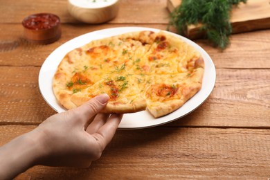 Photo of Woman taking piece of delicious khachapuri with cheese and dill at wooden table, closeup