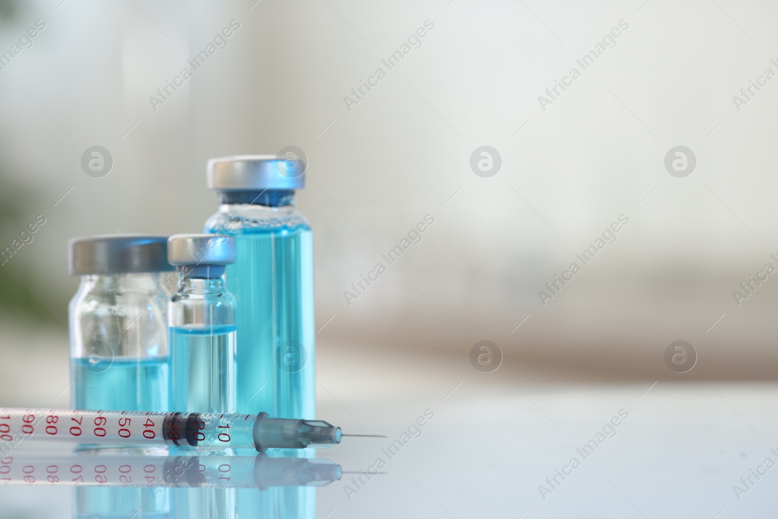 Photo of Glass vials with light blue medication and syringe on white table, closeup. Space for text