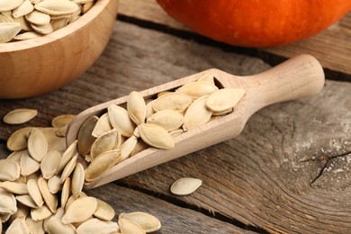 Scoop with pumpkin seeds on wooden table, closeup