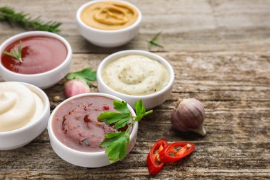 Photo of Different tasty sauces in bowls, herbs and spices on wooden table, closeup