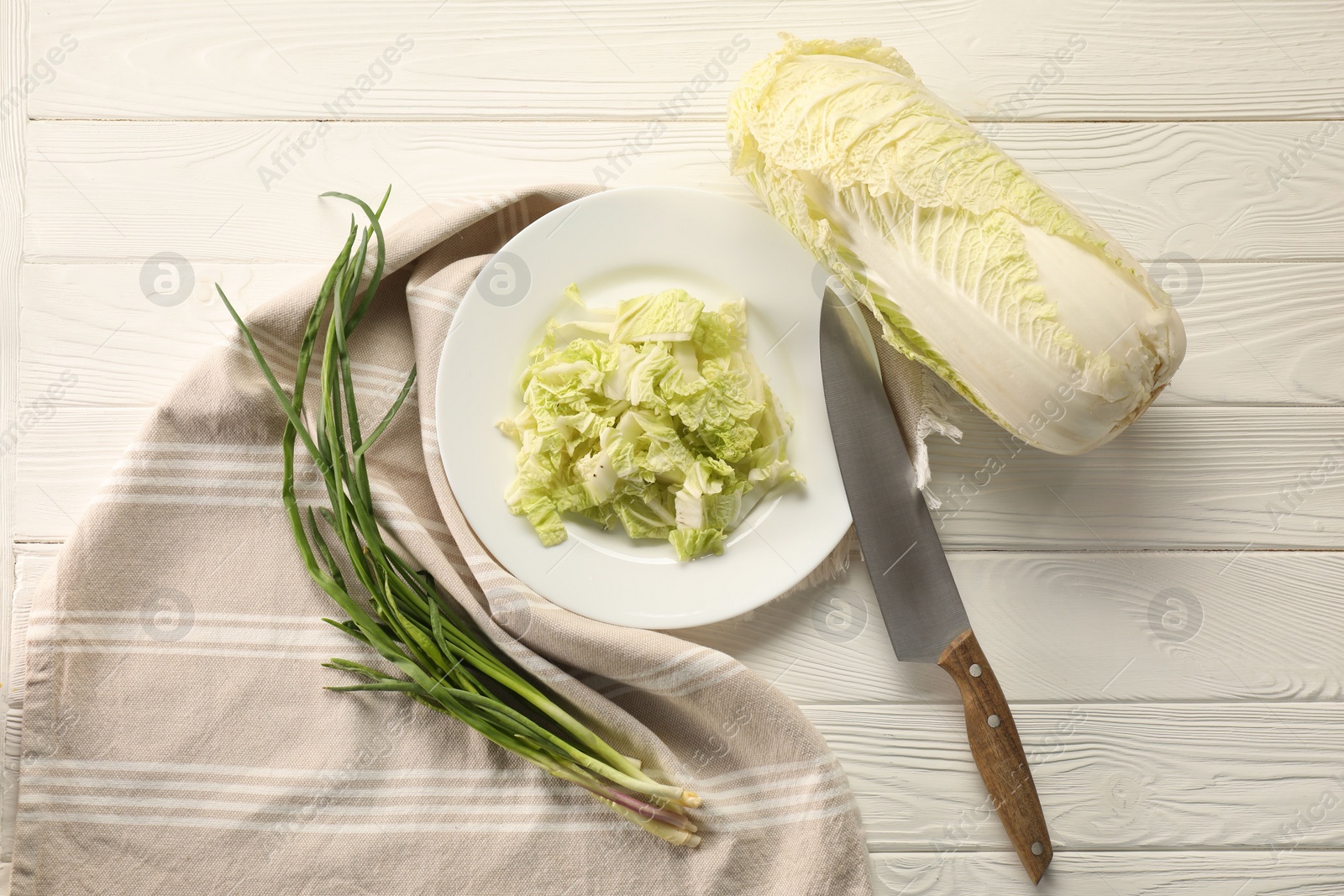 Photo of Fresh Chinese cabbage, green onion and knife on white wooden table, flat lay