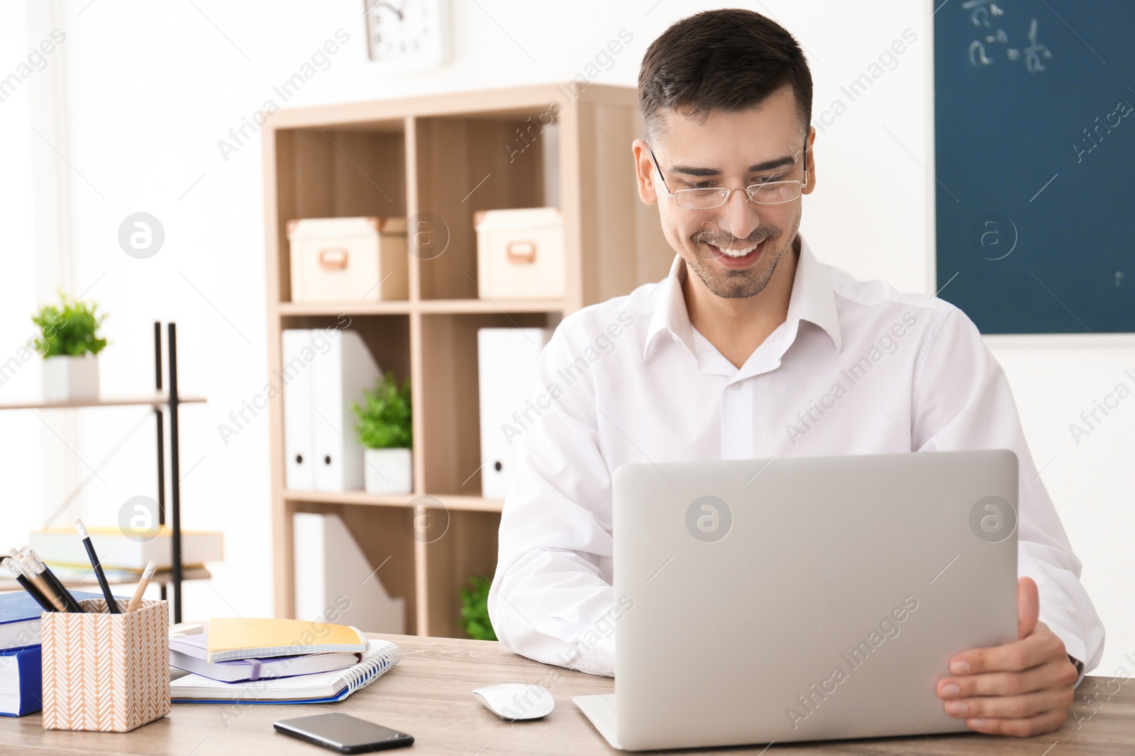 Photo of Young male teacher with laptop sitting at table in classroom