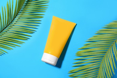 Photo of Sunscreen and tropical leaves on light blue background, flat lay. Sun protection care