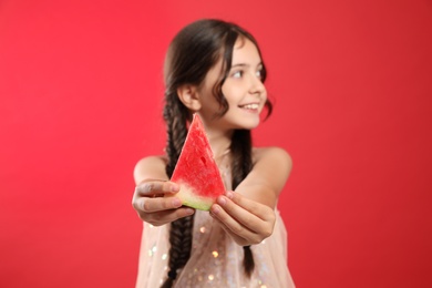 Photo of Cute little girl against red background, focus on hands with watermelon