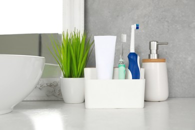 Photo of Electric toothbrushes and tube of paste on white countertop in bathroom