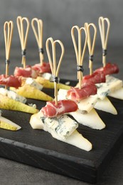 Tasty canapes with pears, blue cheese and prosciutto on grey table, closeup