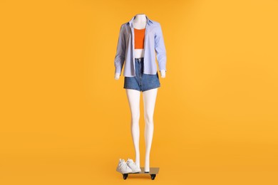 Photo of Female mannequin with sneakers dressed in tank top, striped shirt and denim shorts on orange background. Stylish outfit