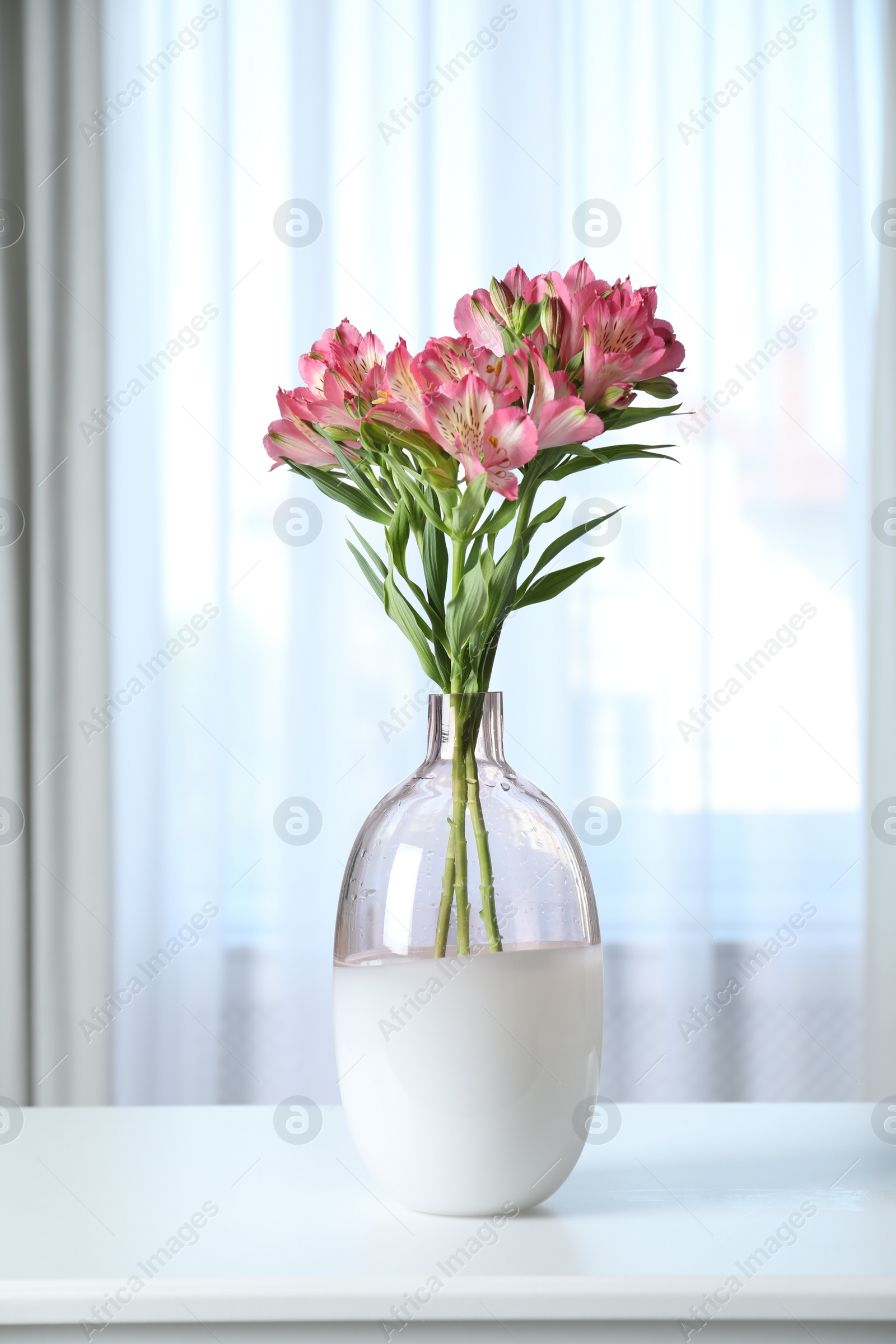 Photo of Vase with beautiful alstroemeria flowers on table near window indoors. Stylish element of interior design