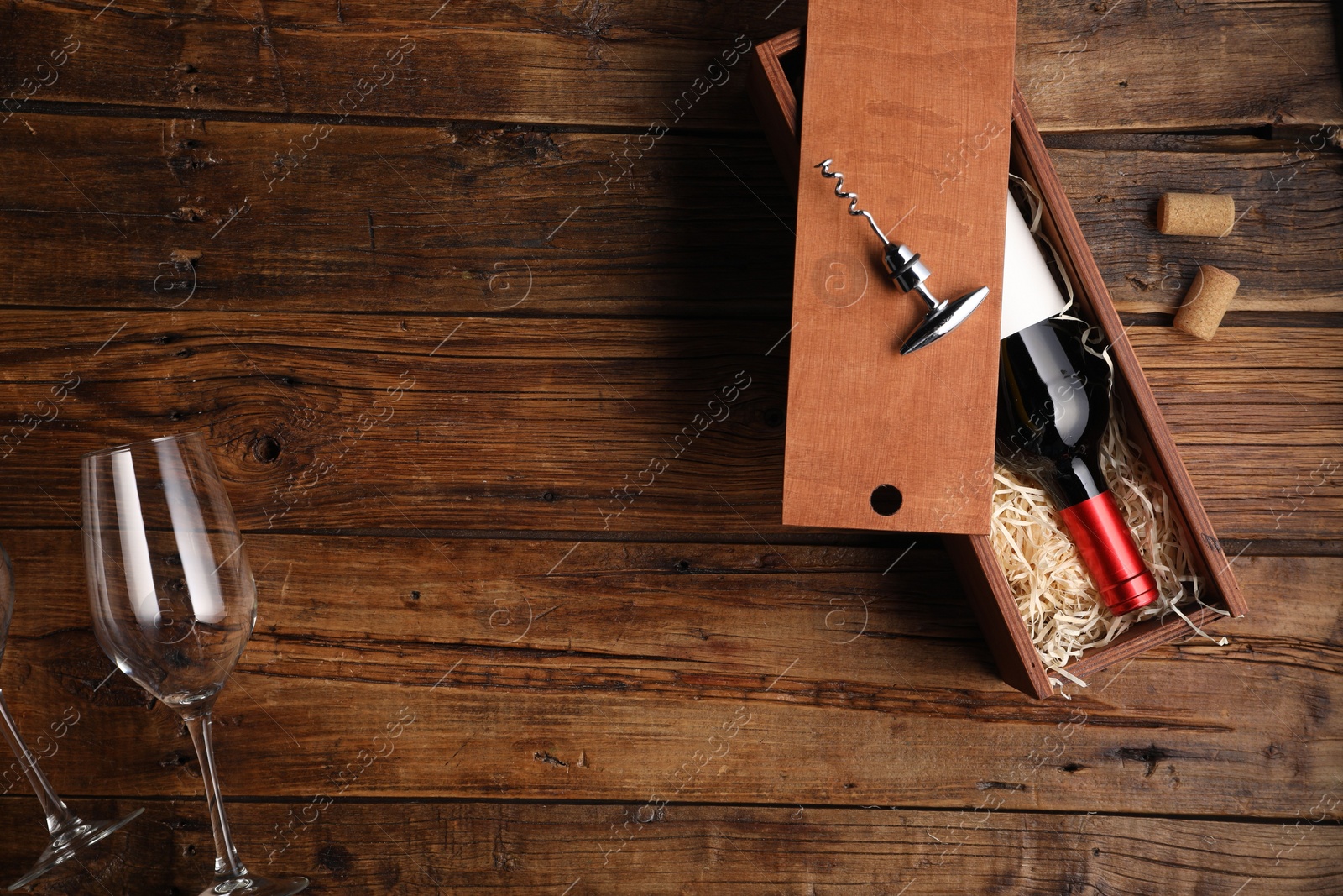 Photo of Box with wine bottle, glasses, corkscrew and corks on wooden table, flat lay