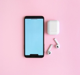 Photo of Wireless earphones, mobile phone and charging case on pink background, flat lay. Space for text