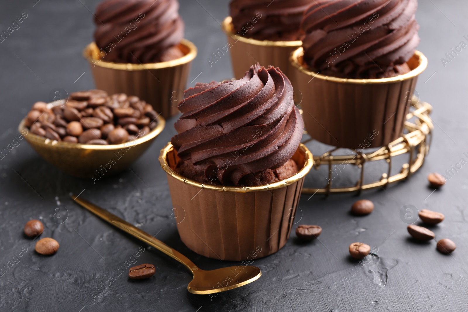 Photo of Delicious chocolate cupcakes and coffee beans on black textured table, closeup