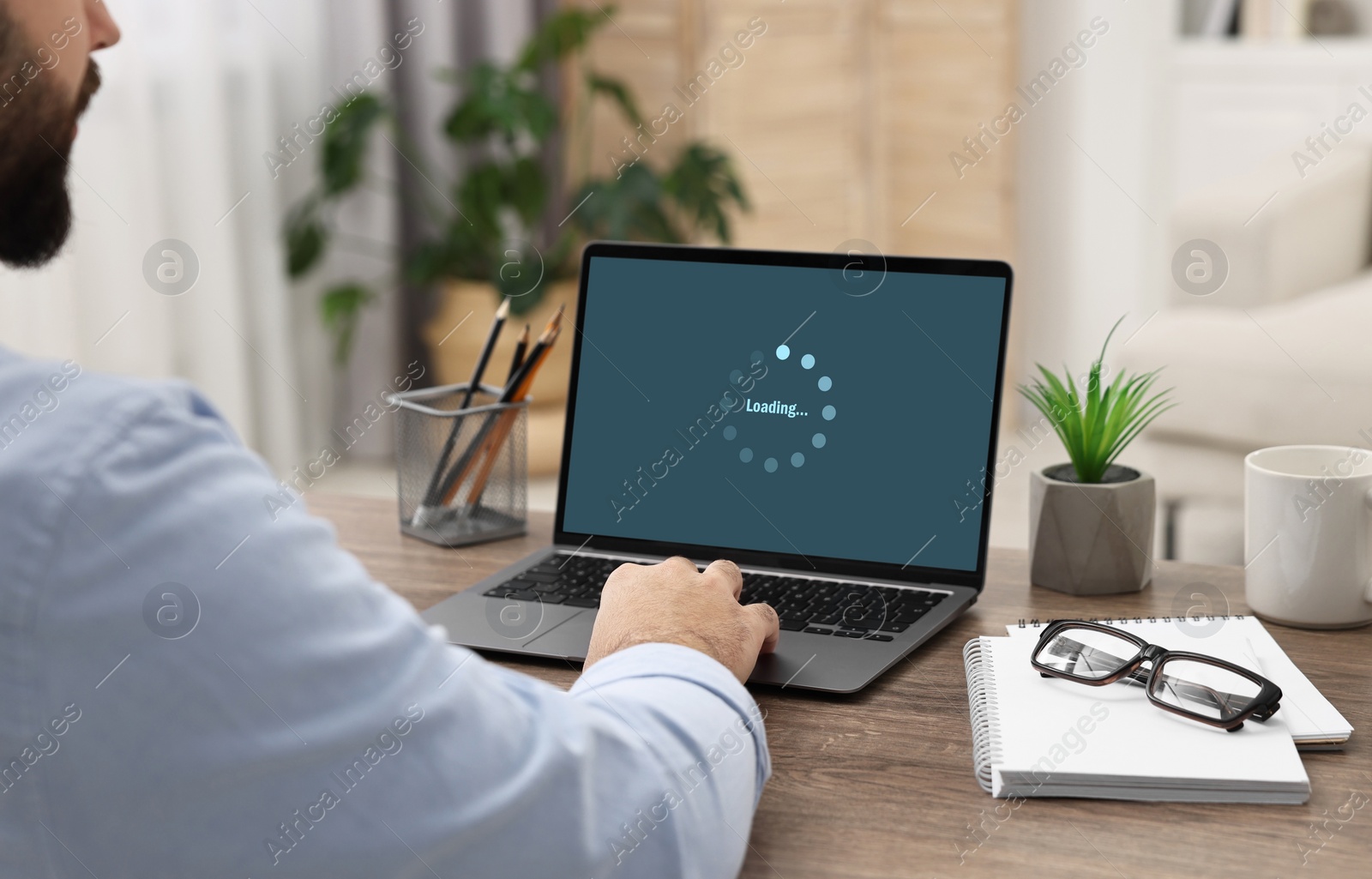 Image of Loading screen displaying progress. Man working on laptop at table indoors, closeup