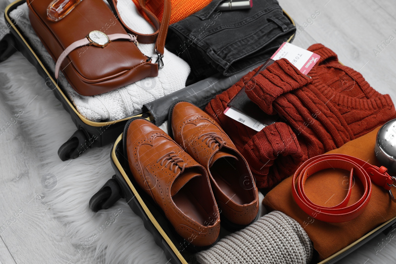 Photo of Open suitcase with folded clothes, accessories and shoes on floor, closeup