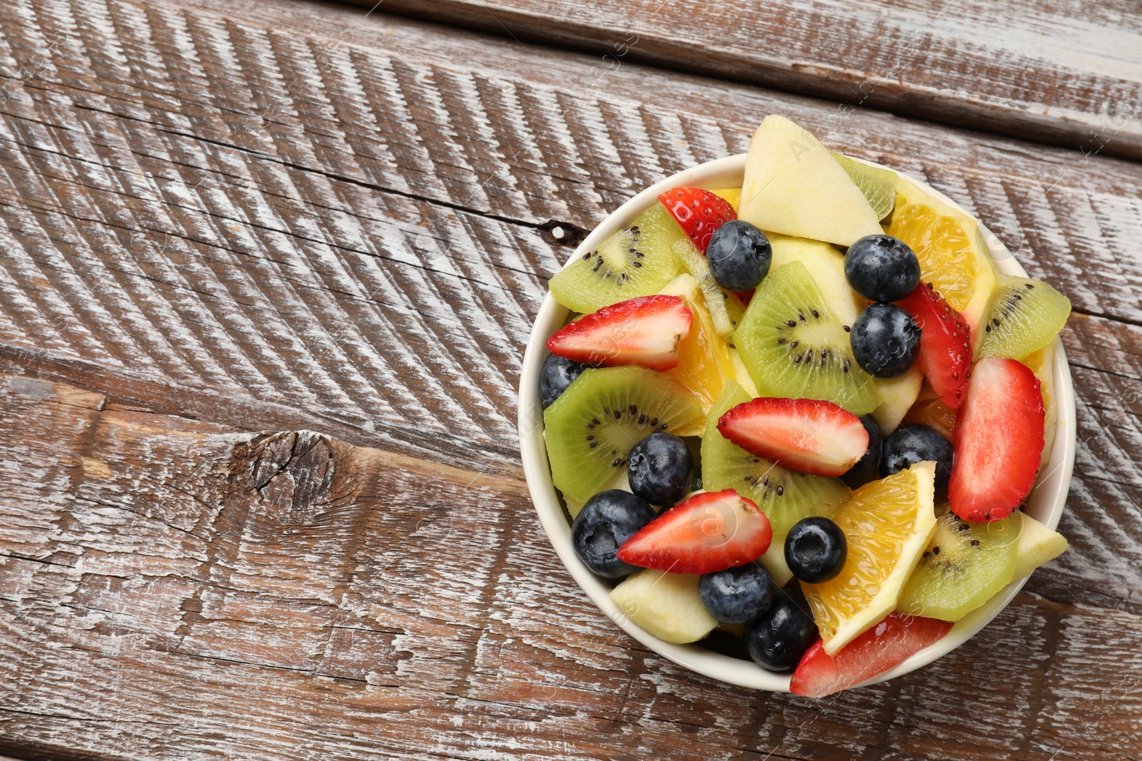 Photo of Tasty fruit salad in bowl on wooden table, top view. Space for text