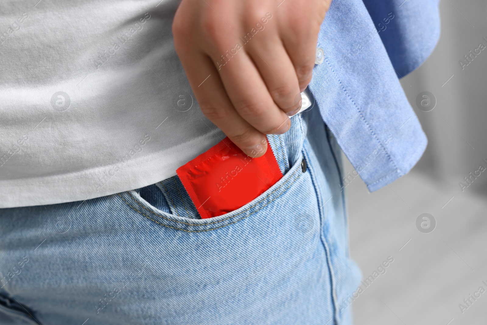 Photo of Man pulling condom out of pocket on blurred background, closeup