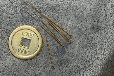 Photo of Acupuncture needles and Chinese coin on grey textured table, flat lay. Space for text