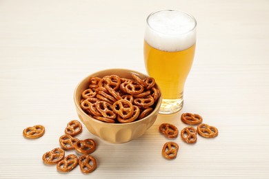 Photo of Delicious pretzel crackers and glass of beer on white wooden table