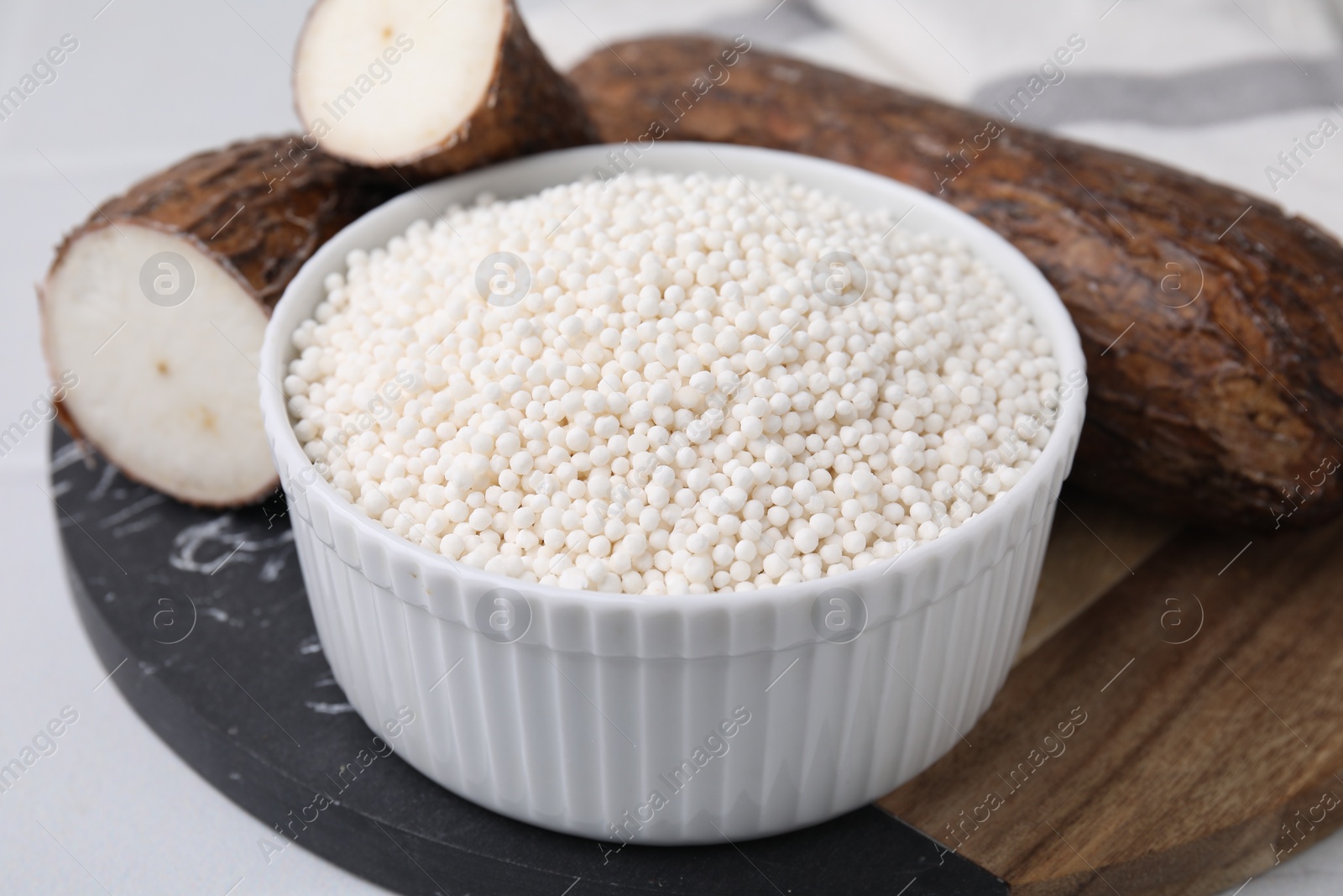 Photo of Tapioca pearls in bowl and cassava roots on table, closeup