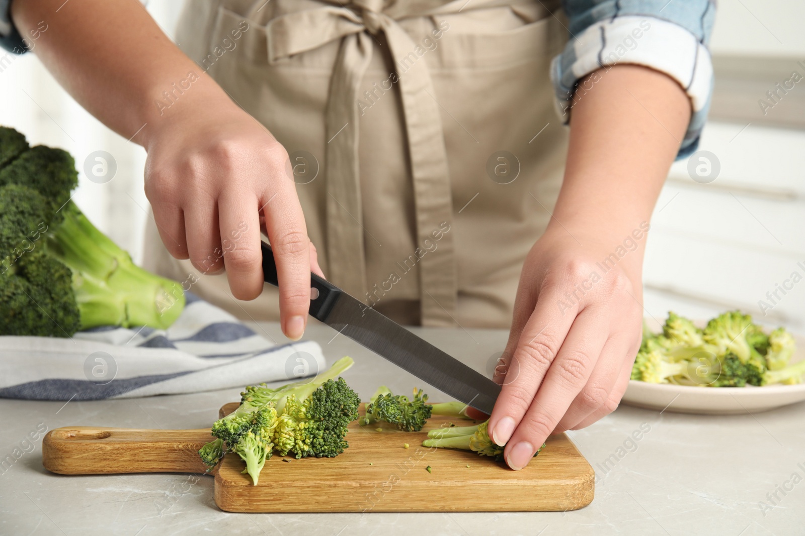 Photo of Woman cutting raw broccoli at light grey marble table, closeup