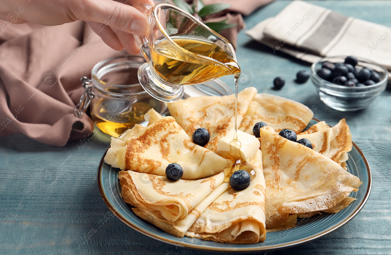 Photo of Woman pouring honey on thin pancakes with berries and butter, closeup