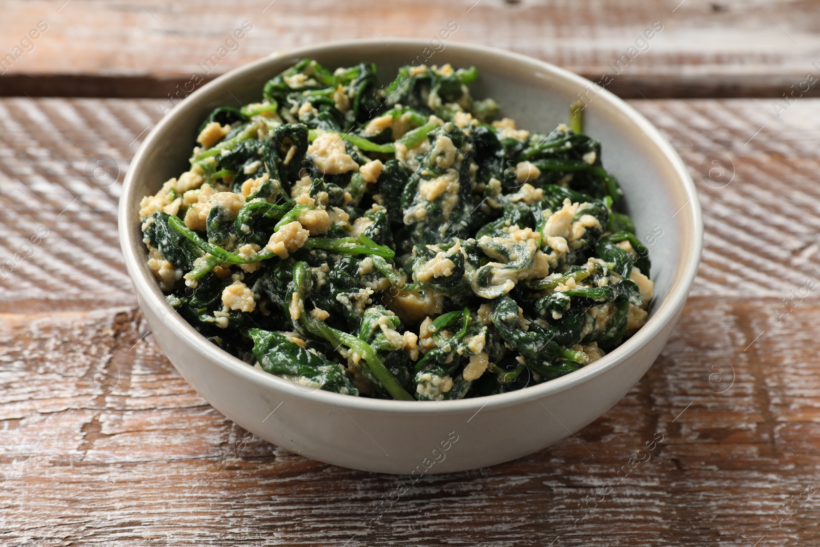 Photo of Tasty spinach dip with egg in bowl on wooden table, closeup