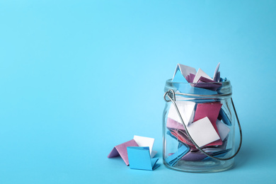Photo of Glass jar full of folded paper sheets on light blue background, space for text