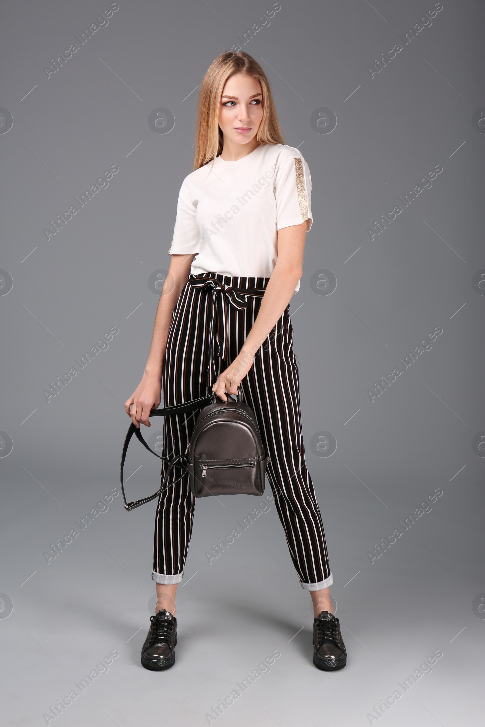 Photo of Young stylish woman in trendy sport shoes with backpack on grey background