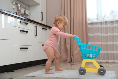 Photo of Cute baby with toy walker in kitchen near window. Learning to walk
