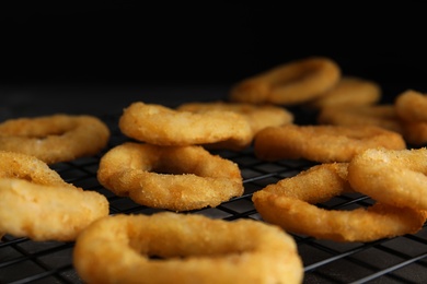Photo of Cooling rack with fried onion rings on table, closeup