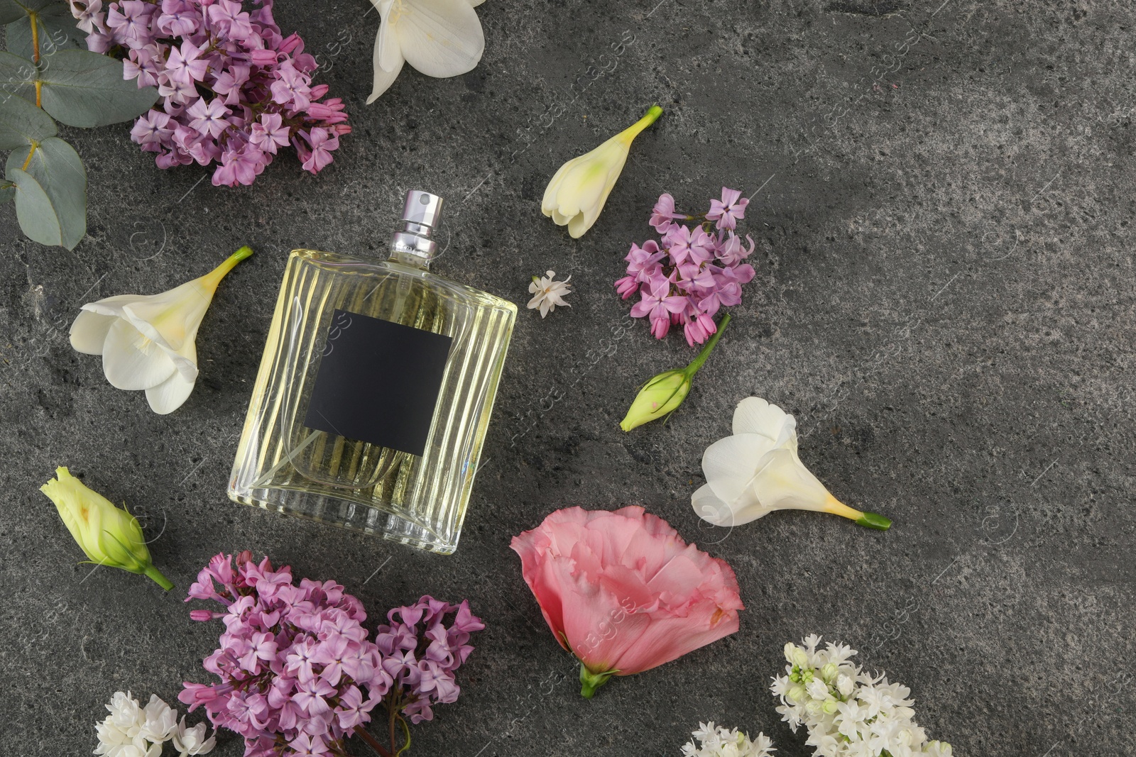 Photo of Bottle of luxury perfume and floral decor on dark grey table, flat lay. Space for text