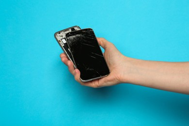 Photo of Woman holding damaged smartphone on light blue background, closeup. Device repairing
