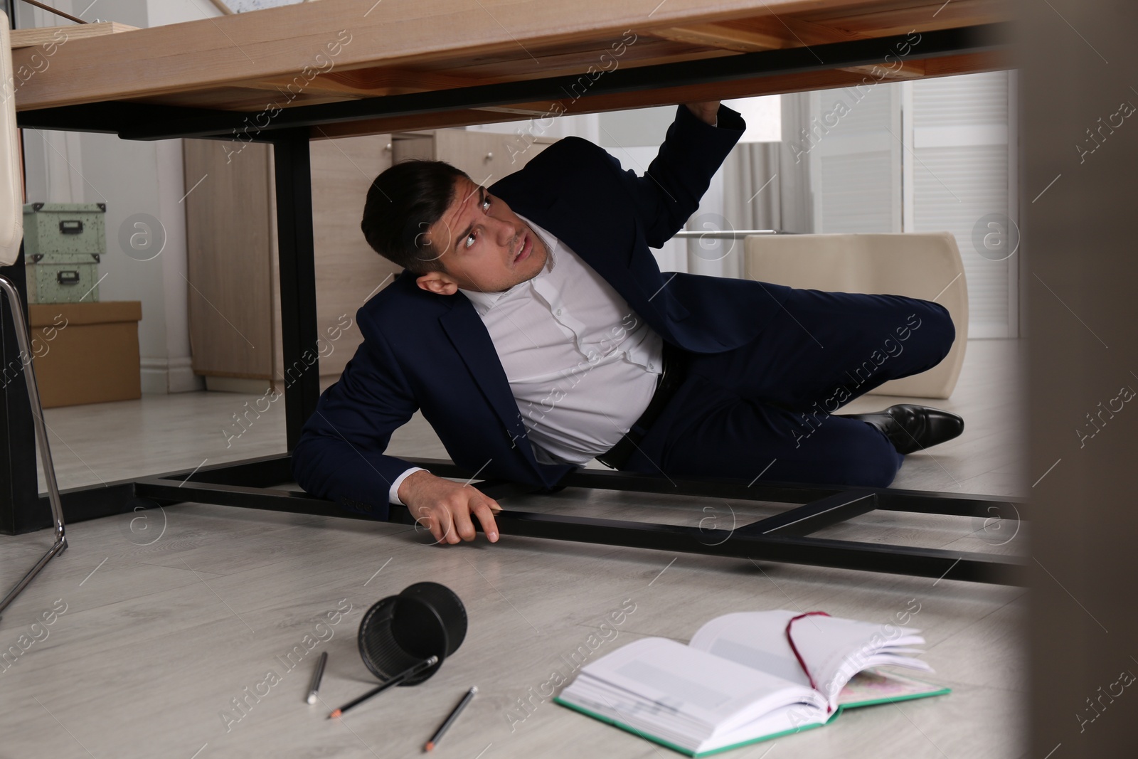 Photo of Scared man hiding under office desk during earthquake