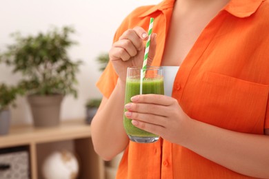 Woman holding glass with delicious smoothie indoors, closeup