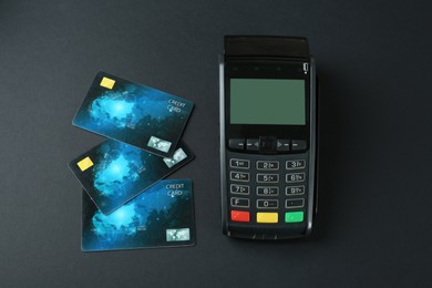 Photo of New modern payment terminal and credit cards on black background, flat lay