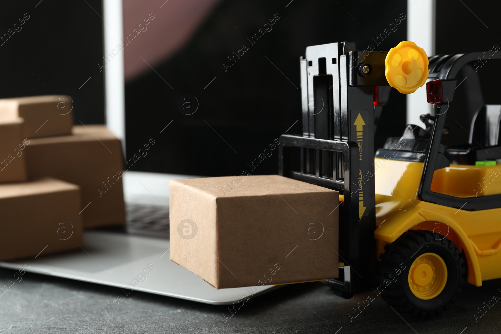 Photo of Toy forklift with box near laptop on table. Logistics and wholesale concept