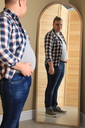 Photo of Overweight man in tight t-shirt near mirror at home