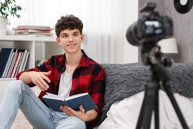 Smiling teenage blogger reading book while streaming at home