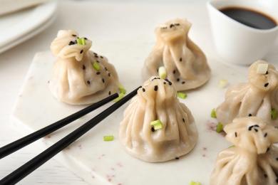 Board with tasty baozi dumplings and chopsticks on table, closeup