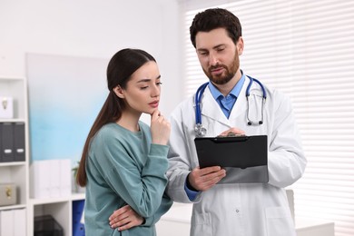 Photo of Doctor with clipboard consulting patient during appointment in clinic