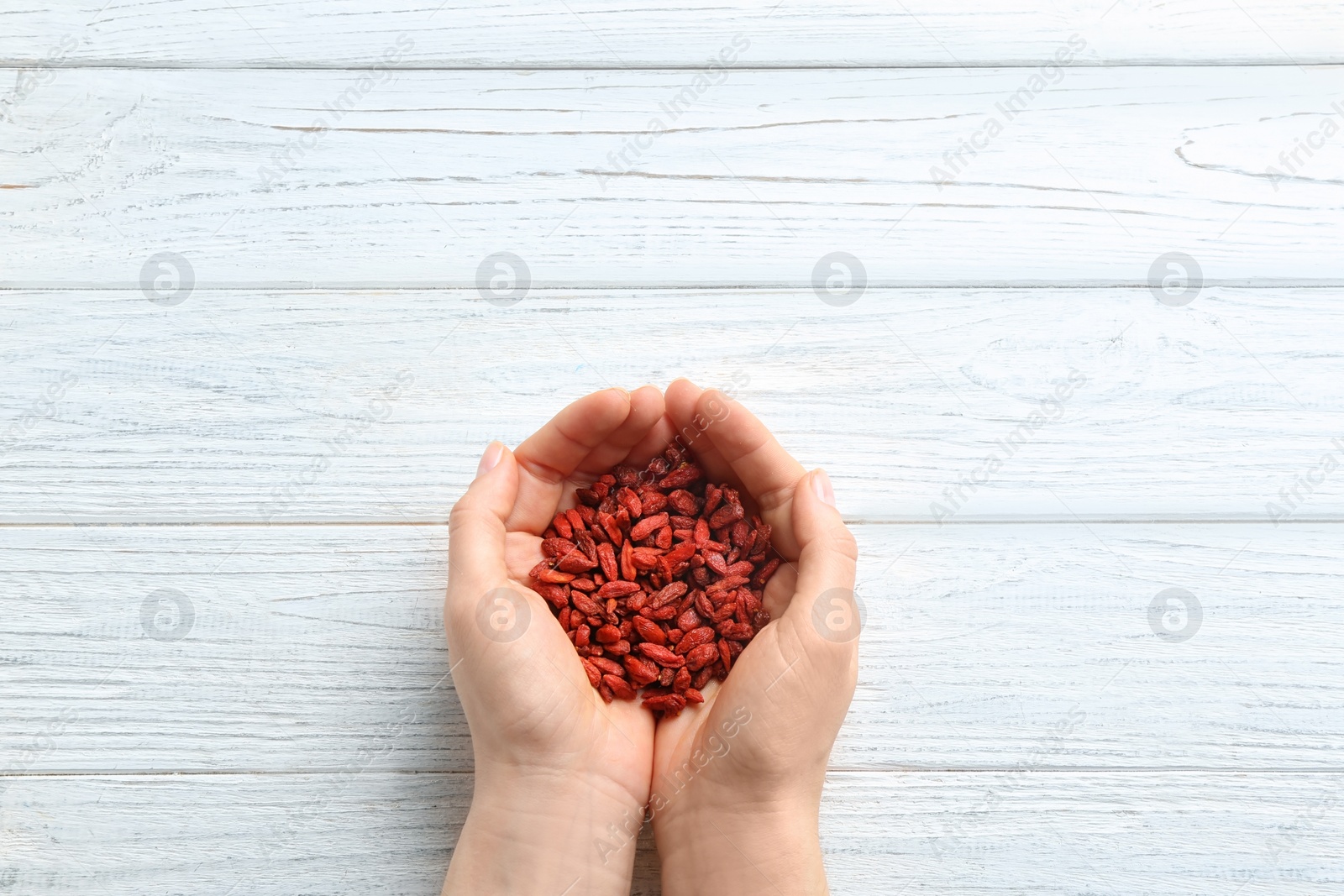 Photo of Woman holding red dried goji berries on white wooden background, top view