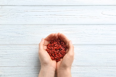 Photo of Woman holding red dried goji berries on white wooden background, top view