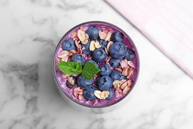 Photo of Glass of delicious blueberry smoothie with granola and mint on white marble table, top view