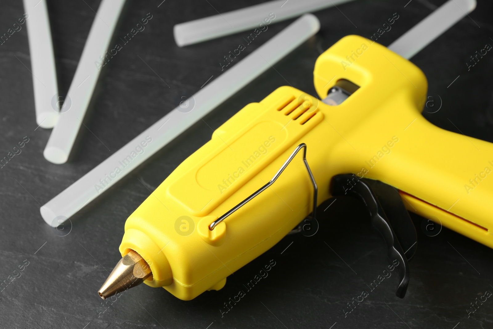 Photo of Hot glue gun and sticks on dark grey table, closeup