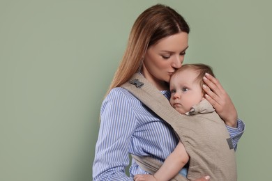 Photo of Mother holding her child in sling (baby carrier) on olive background. Space for text