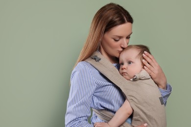 Mother holding her child in sling (baby carrier) on olive background. Space for text