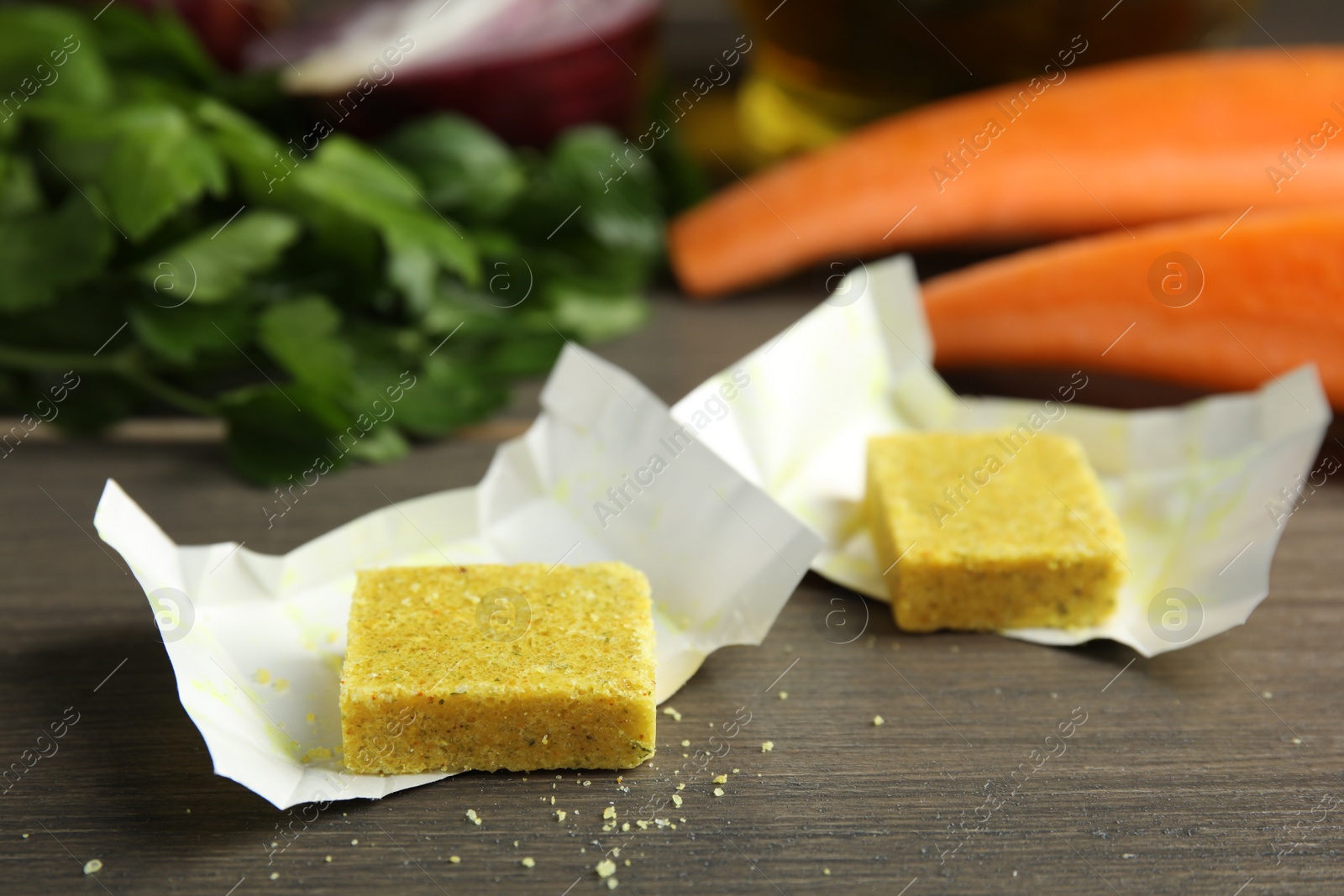 Photo of Bouillon cubes and other ingredients for soup on wooden table, closeup